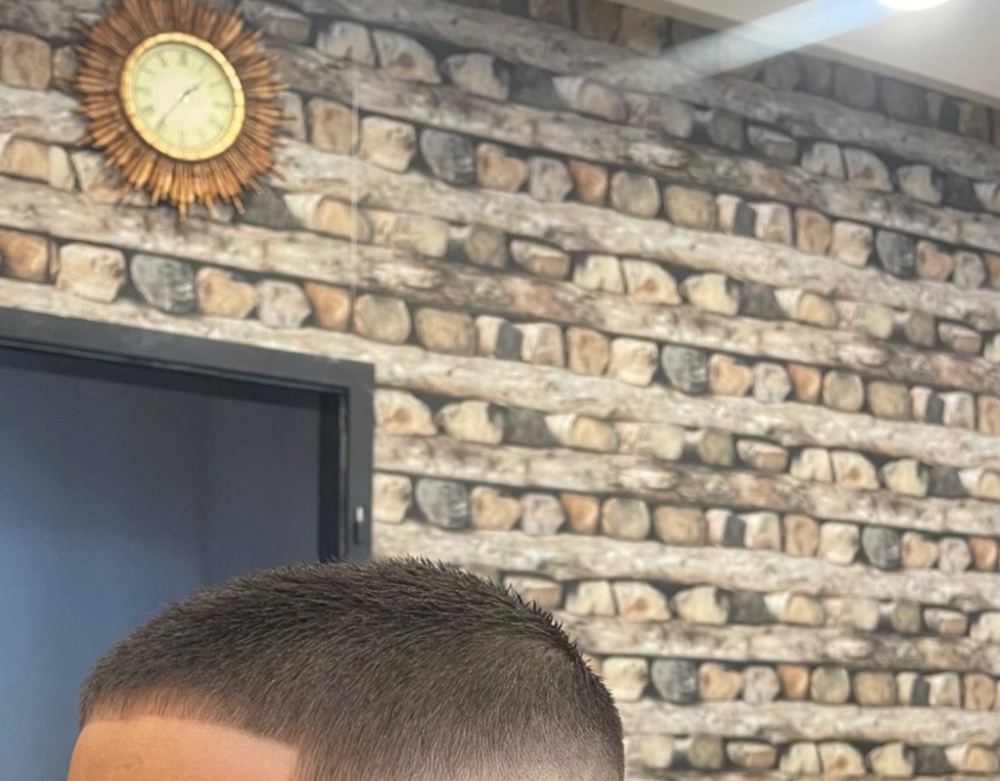 Kurzer Schnitt mit Skin Fade vor der Natursteinwand und der Sonnenuhr
